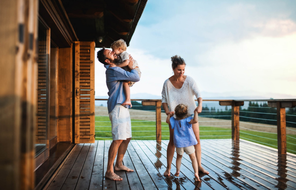 Family-with-small-children-playing-in-rain-on-patio-by-wooden-cabin-holiday-in-nature-concept